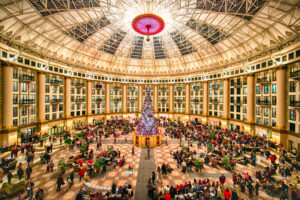 A huge hall-dome filled with people and a very lit up Christmas tree.