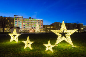 Decorative stars outside the hotel on a lawn standing far in front of another very lit Christmas tree.