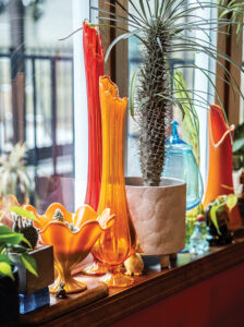 Various vintage glass items, colored orange and red, on display on a windowsill in Sara Rhoades' home. A cactus is also on the windowsill.