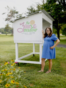 Photo of Ellie Ziliak at sign for The Zinnia Meadow by Brodie Curtsinger