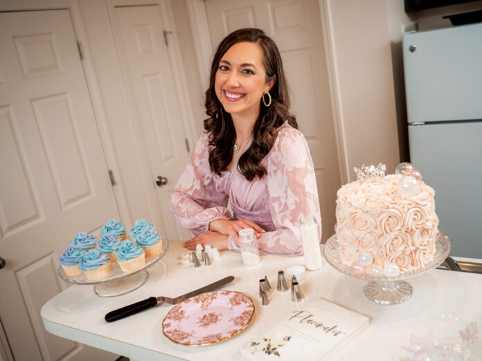 Mallory Pleiss stands in her kitchen with an intricately decorated buttercream frosting cake from her business, Icing On The Cake