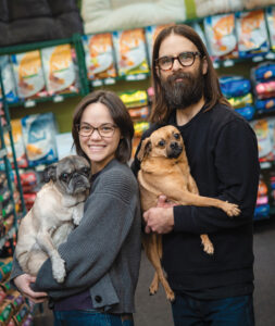 Two people standing together and holding pugs in their arms