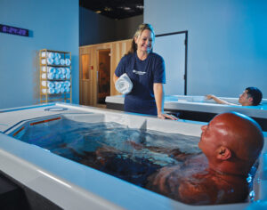 Woman talks to man submerged in tub of cold water